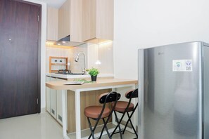 Eine kompakte Küche mit einem Edelstahl-Kühlschrank, Holzschränken, einer kleinen Kochinsel mit Barhocker und einem Spülbecken mit Armatur.
