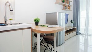 A modern kitchen with a built-in sink, a stainless steel refrigerator, a wooden dining table, and a small potted plant. - 2 Pax Serene Studio At Lrt City Bekasi Apartment (Bekasi)
