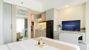 Ett hotellrum med en säng, ett skrivbord, en tv, ett litet kök och ett badrum.