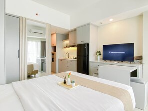 A hotel room with a bed, a desk, a television, a kitchen area, and a bathroom. - Relaxing Studio Apartment At Lrt City Jatibening (Bekasi)