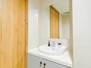 A bathroom with a wooden door, a white sink, a mirror, and a small potted plant. - Relaxing Studio Apartment At Lrt City Jatibening (Bekasi)