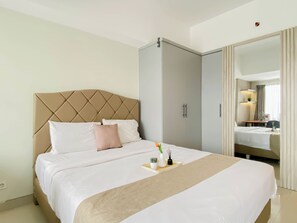 Quarto de hotel com uma cama, guarda-roupa, espelho e uma mesinha com um vaso e uma planta.
