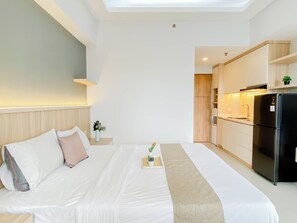 Ein Hotelzimmer mit Bett, Nachttisch mit Vase, Küchenzeile mit Kühlschrank und Spüle.
