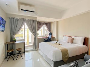 Ein Hotelzimmer mit Bett, Schreibtisch, zwei Stühlen, einem Fernseher und einer Klimaanlage.