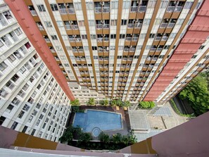 Ein Hochhaus mit Wohneinheiten, mehreren Balkonen, einem Pool auf dem Dach und umliegendem Grün.