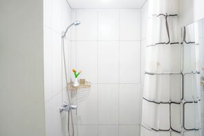 Eine Dusche mit Handbrause, Handtuchhalter und einem kleinen Ablagebereich mit einer Vase und Blumen.