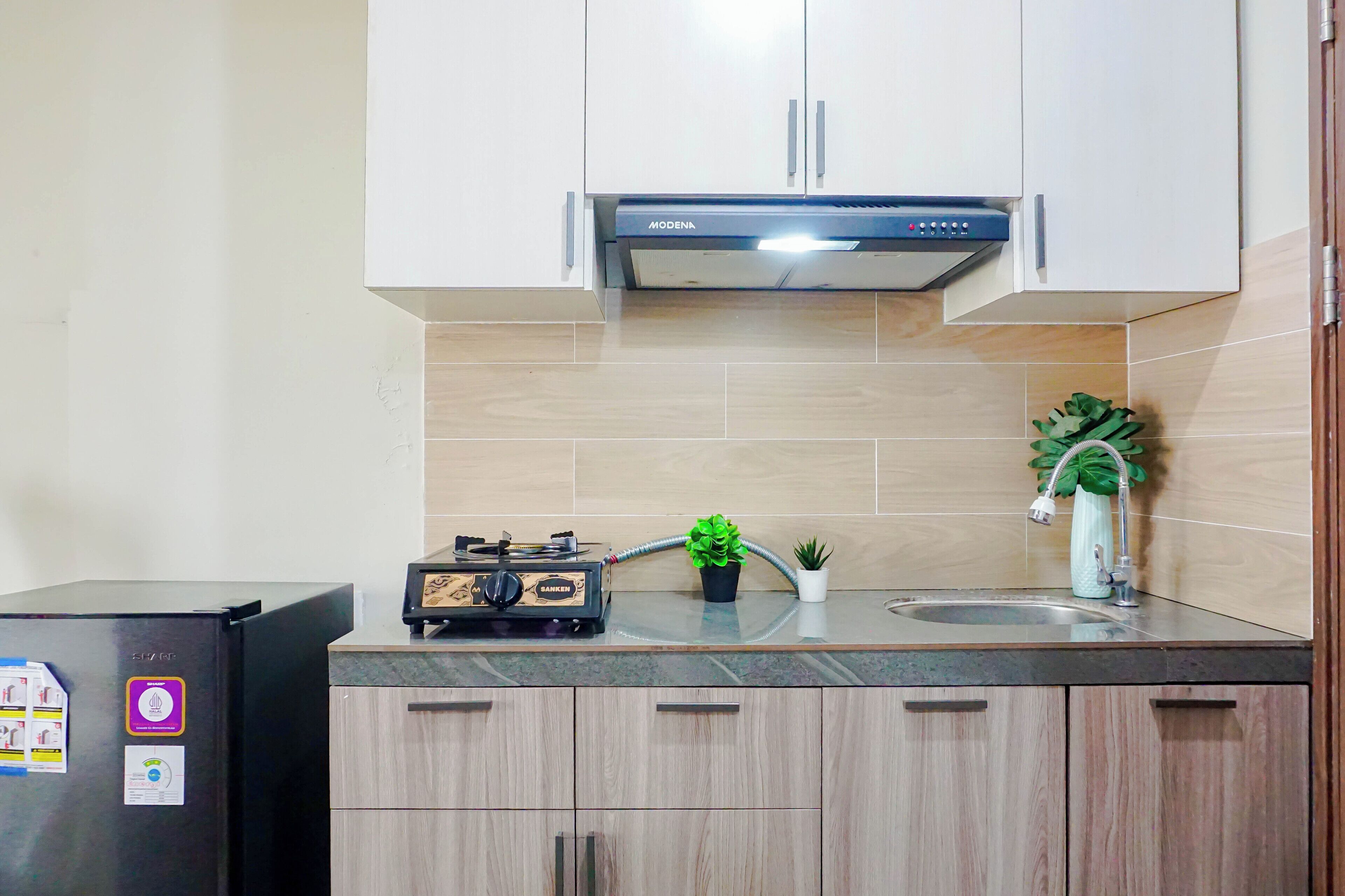 Una cocina con un refrigerador negro, estufa a gas, gabinetes, un lavamanos y una campana de ventilación.