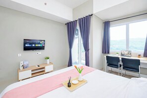 A hotel room with a bed, desk, chairs, a TV, and a view of the outdoors. - Studio Near Bellanova Country Mall At Royal Sentul Park Apartment (Bogor)