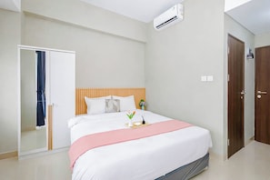 A bedroom with a bed, a bedside table, an air conditioning unit, and a wardrobe. - Studio Near Bellanova Country Mall At Royal Sentul Park Apartment (Bogor)