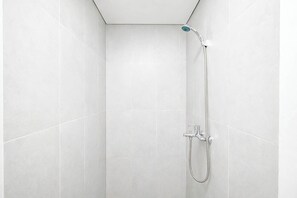 A shower with a handheld showerhead and a wall-mounted faucet in a tiled bathroom. - Studio Near Bellanova Country Mall At Royal Sentul Park Apartment (Bogor)