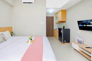 Ein Hotelzimmer mit Bett, Fernseher, Küchenzeile und kleinem Schreibtisch.
