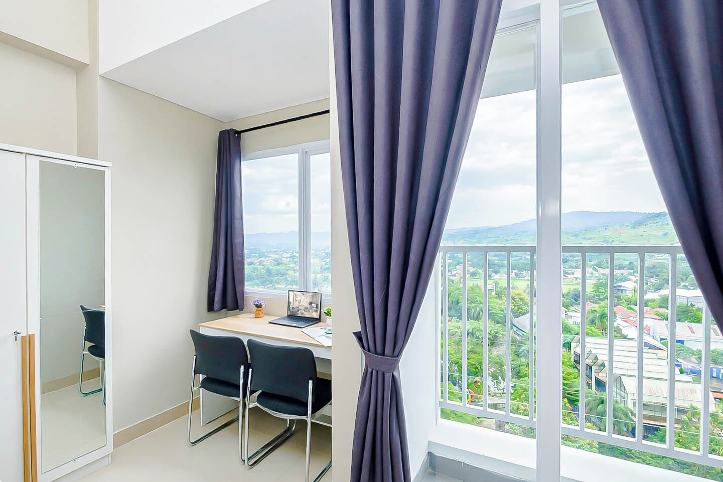 Ein Zimmer mit Schreibtisch, zwei Stühlen, einem Laptop und Blick auf eine grüne Landschaft durch große Fenster.