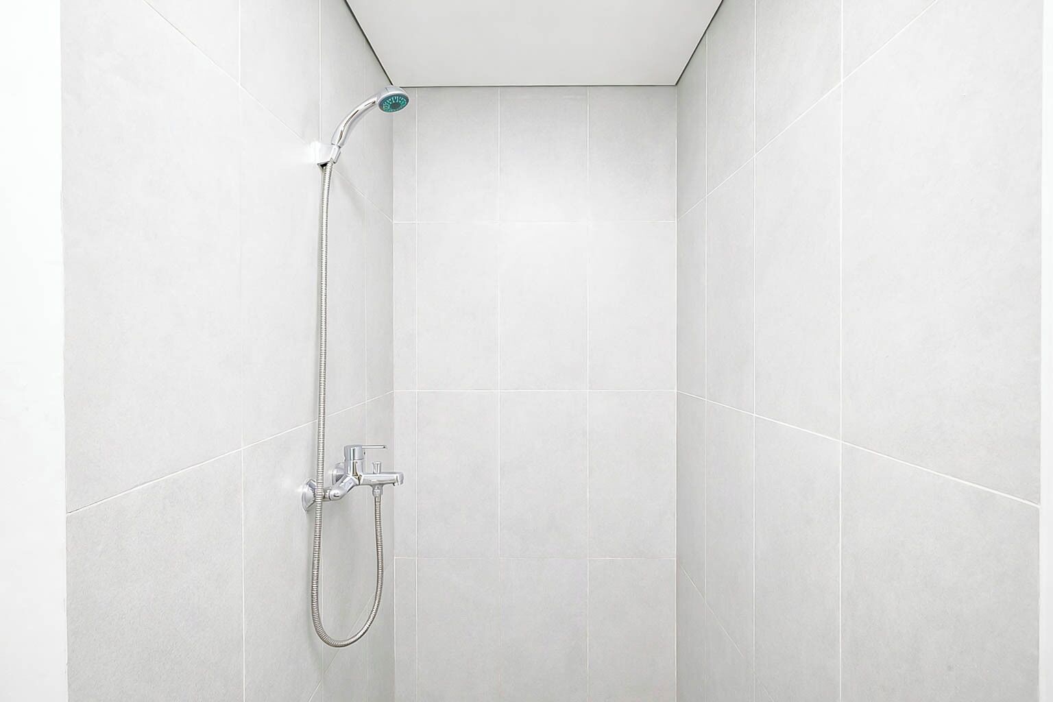 A shower with a handheld showerhead and a wall-mounted faucet in a tiled room.