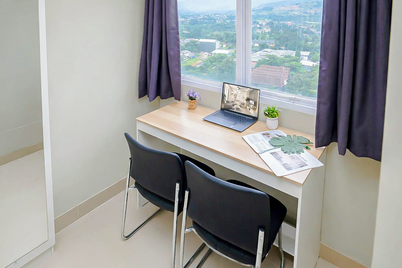 A small office space with a desk, two chairs, a laptop, a potted plant, and a window with curtains.
