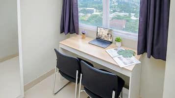 A small office space with a desk, two chairs, a laptop, a potted plant, and a window with curtains.