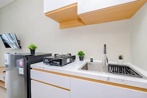 A modern kitchen with a built-in refrigerator, a sink, a small island, and a flat-screen TV mounted on the wall. - Restful Studio With City View At Royal Sentul Park Apartment (Bogor)