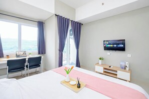 Ein Hotelzimmer mit einem Bett, einem Schreibtisch mit zwei Stühlen, einem Fernseher und einem Fenster mit Vorhängen.