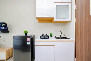 A compact kitchen with white cabinets, a black refrigerator, a small sink, and a flat-screen TV mounted on the wall.