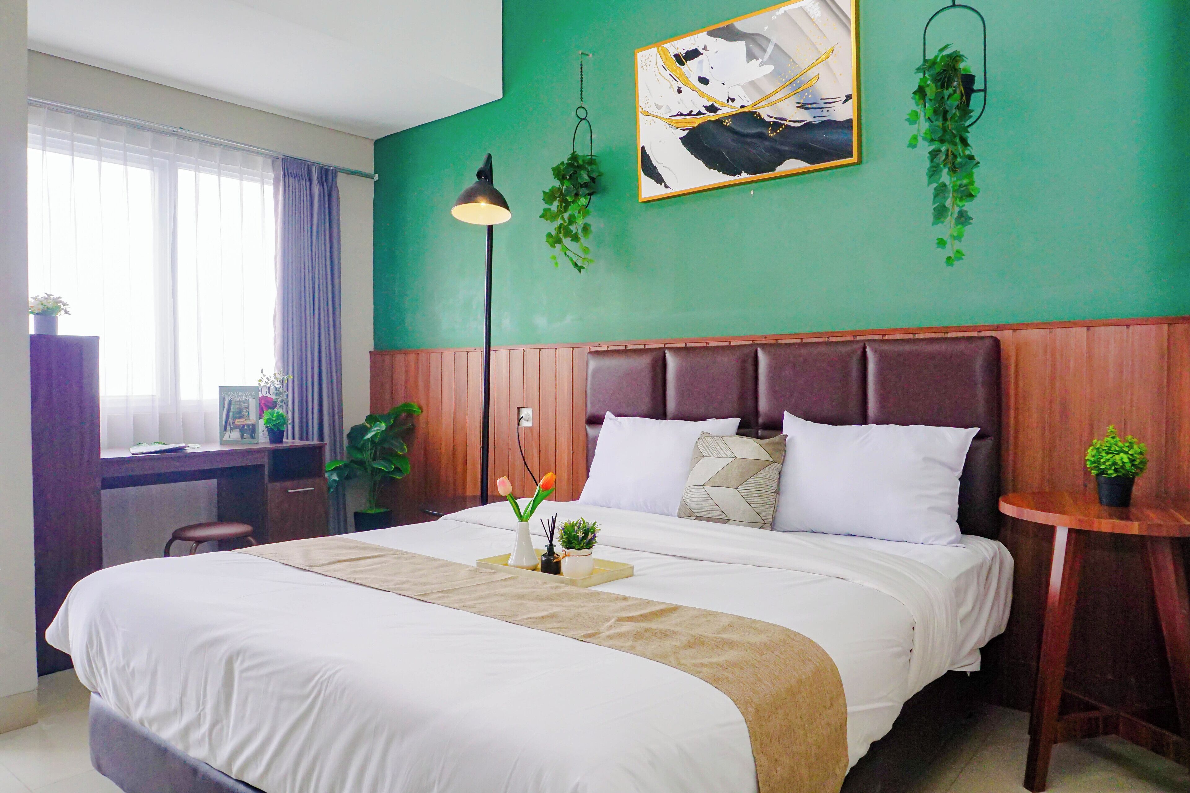 Una habitación de hotel con una cama grande, un escritorio, una silla, una mesita y una planta en maceta.
