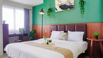 Una habitación de hotel con una cama grande, un escritorio, una silla, una mesita y una planta en maceta.