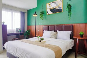 Quarto de hotel com uma cama grande, uma escrivaninha, uma cadeira, uma mesinha e um vaso de plantas.