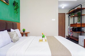Une chambre d’hôtel comprenant un lit, une table de chevet, une petite plante en pot, un four à micro-ondes et une étagère avec une plante.