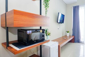 Una habitación moderna con un microondas en un estante de madera, un refrigerador pequeño, un televisor montado en la pared y una ventana con cortinas.