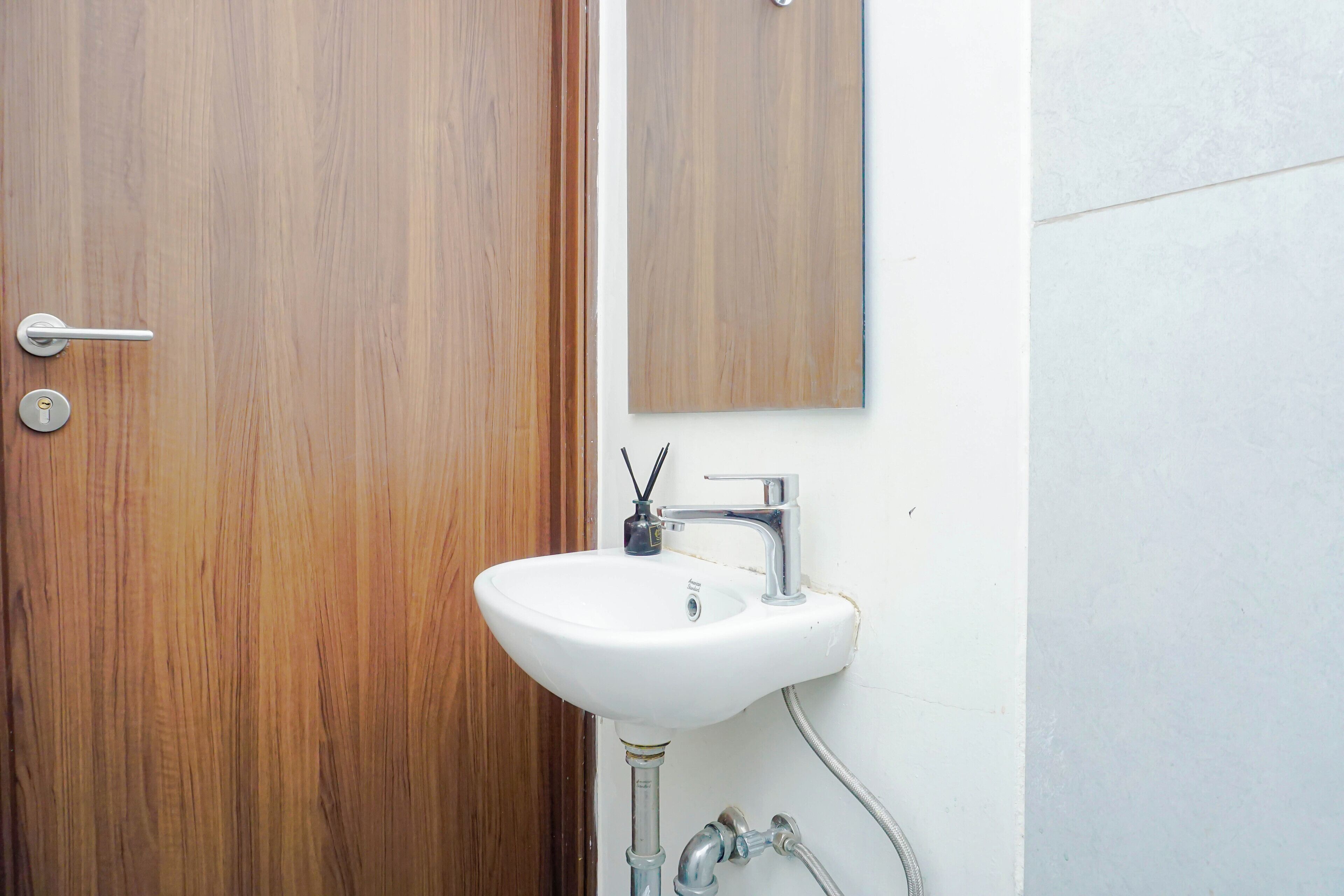 Un baño con puerta de madera, un lavabo blanco y un espejo.