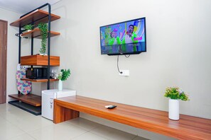 Un salon moderne avec un téléviseur, des étagères en bois, un banc, un petit réfrigérateur et un vase rempli de fleurs.