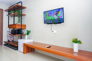A modern living room with a TV, wooden shelves, a bench, a small fridge, and a vase with flowers.