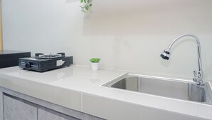 Una cocina con encimera blanca, pileta de acero inoxidable y una pequeña planta en maceta.