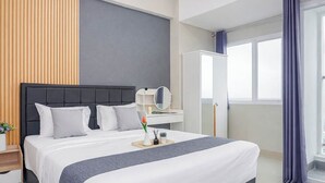 Una habitación de hotel moderna con una cama grande, una mesita de noche con espejo, una planta pequeña y una ventana con cortinas.