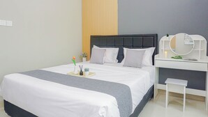 Una cama bien hecha con colcha gris y blanca, una mesita de noche con espejo y un pequeño taburete.
