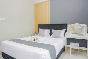 A neatly made bed with a grey and white bedspread, a bedside table with a mirror, and a small stool. - Serene Studio At Royal Sentul Park Apartment (Bogor)