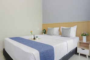 Ein ordentlich bezogenes Bett mit blauen Akzenten, ein Nachttisch mit einer Vase und ein an der Wand befestigtes Regal.