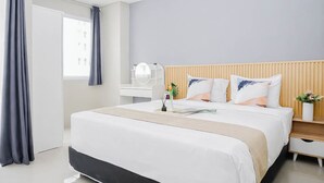 Una habitación de hotel moderna con una cama grande, mesitas de noche, un tocador con espejo y una ventana con cortinas.