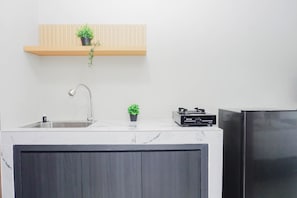 Une cuisine équipée d’un évier, d’une petite plante en pot, d’un chauffe-eau Rinnai et d’un réfrigérateur noir.