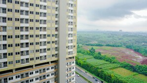 Un edificio alto con varios balcones, una carretera con vehículos y un paisaje verde al fondo.