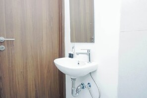A bathroom with a wooden door, a white sink with a mirror above it, and a shower area. - Neat And Restful Studio At Apartment Lrt City Sentul - Royal Sentul Park (Bogor)