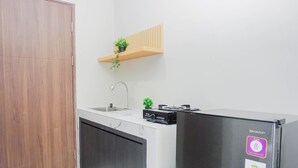 A kitchen with a built-in refrigerator, a sink, and a wooden shelf with a plant. - Neat And Restful Studio At Apartment Lrt City Sentul - Royal Sentul Park (Bogor)