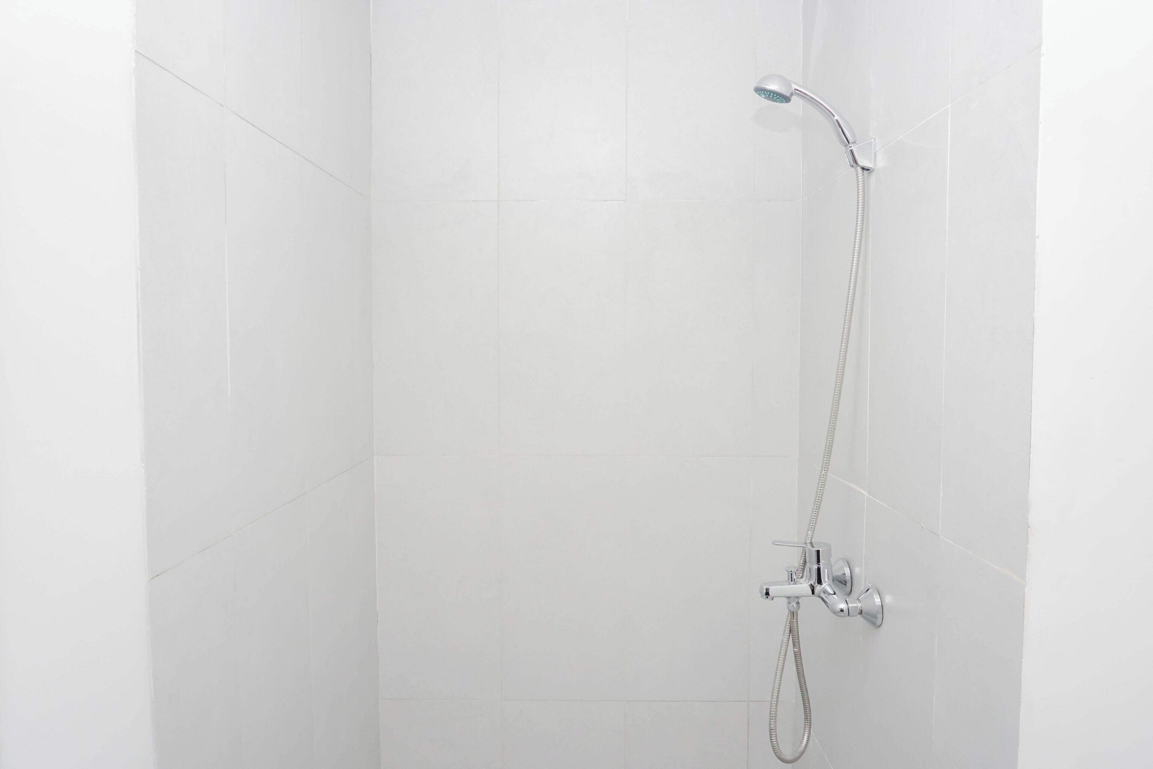 A shower with a handheld showerhead and a wall-mounted faucet in a room with white tiled walls.