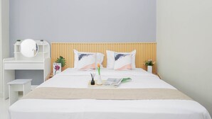 A neatly arranged bedroom with a bed, bedside table, and a small desk with a mirror. - Neat And Restful Studio At Apartment Lrt City Sentul - Royal Sentul Park (Bogor)