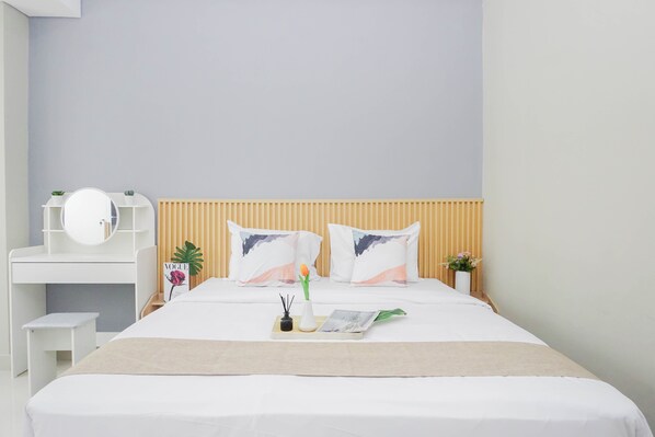 A neatly arranged bedroom with a bed, bedside table, and a small desk with a mirror. - Neat And Restful Studio At Apartment Lrt City Sentul - Royal Sentul Park (Bogor)