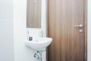 Ein Badezimmer mit einem weißen Waschbecken, einem Spiegel und einer Holztür.