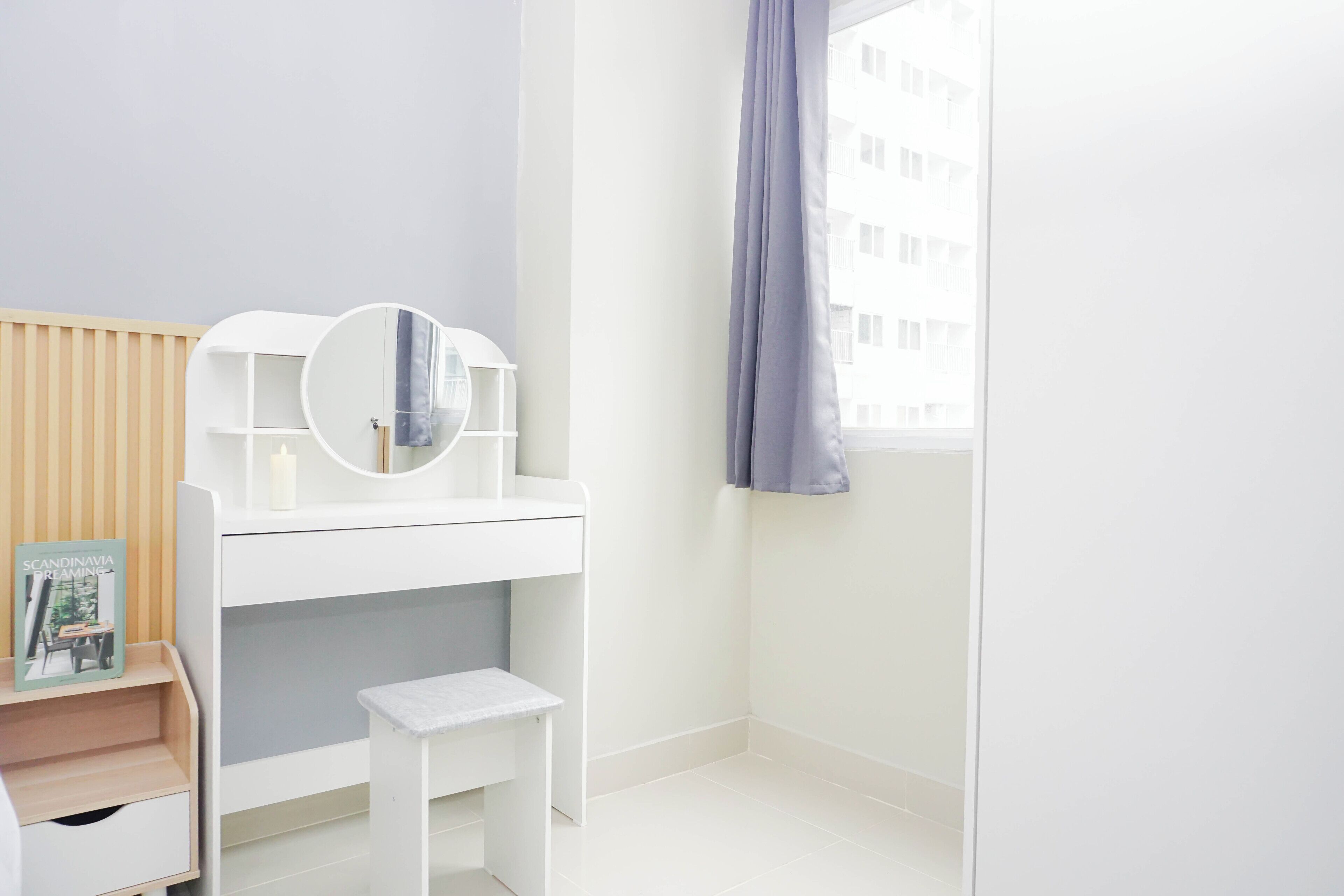 A white vanity with a mirror, a small stool, and a magazine on a shelf.