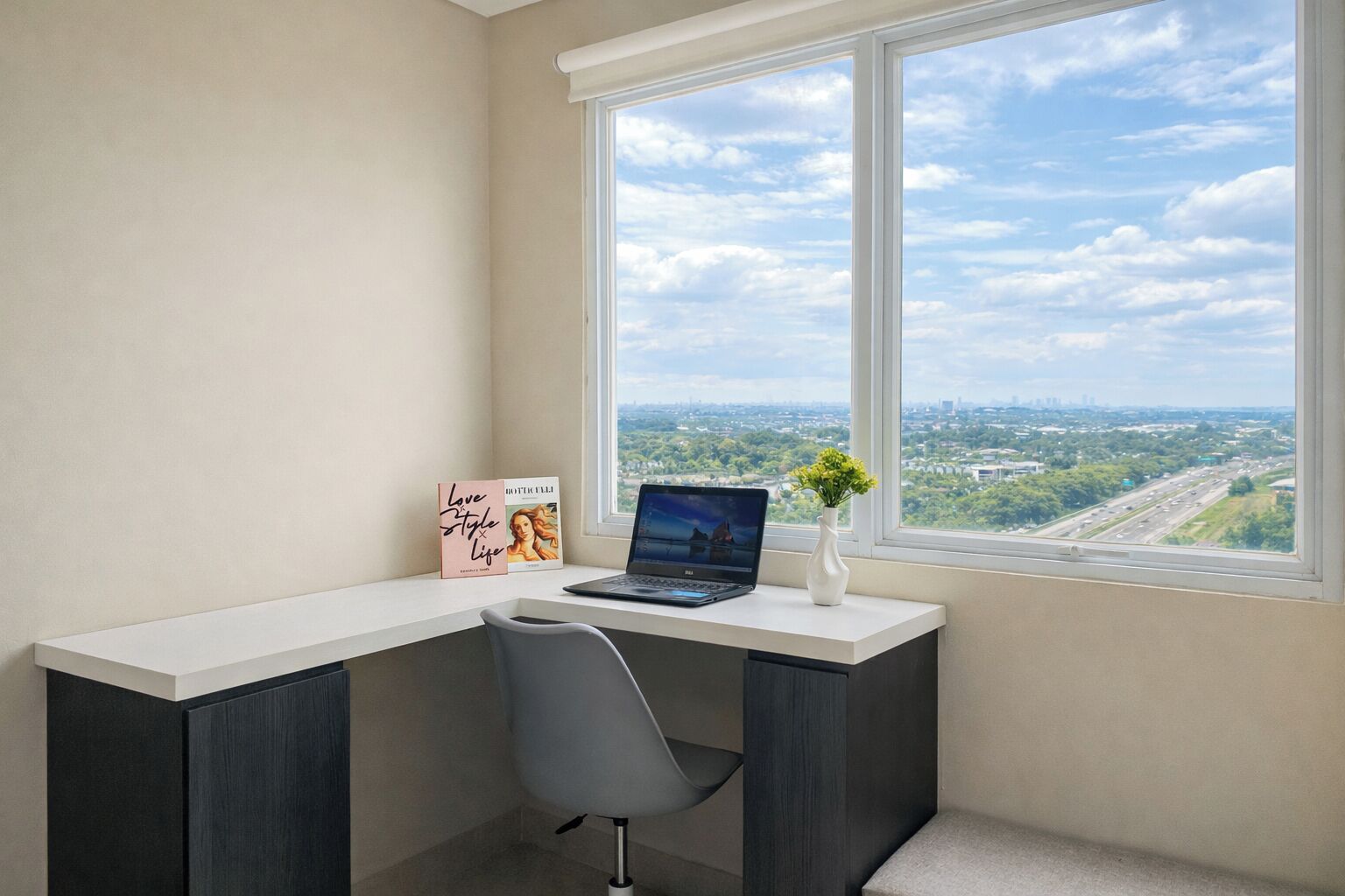 Un bureau d’angle avec un bureau, un ordinateur portable, un vase de fleurs et un livre intitulé « L’art de vivre et d’aimer ».