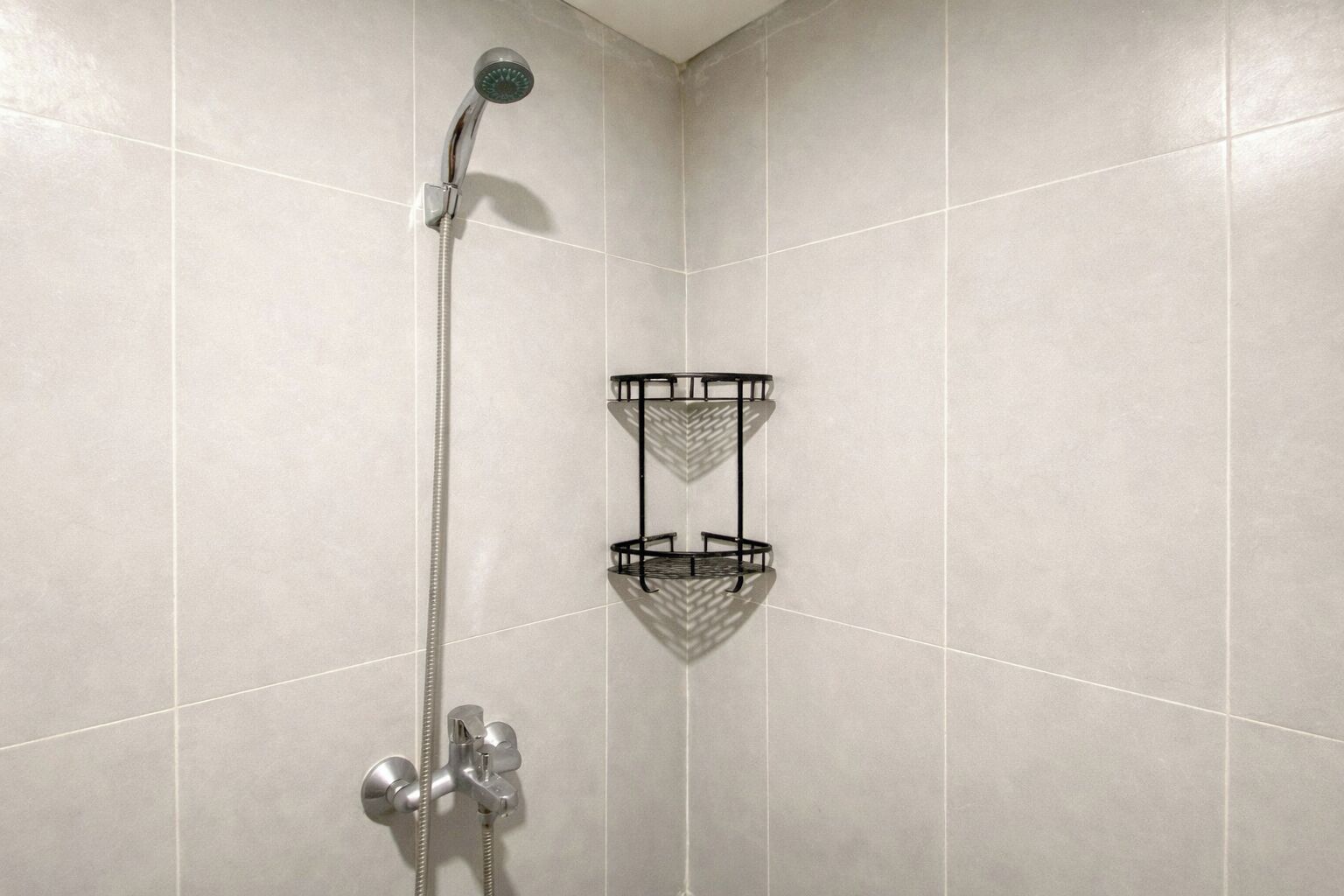 A shower with a handheld showerhead and a wall-mounted faucet. There is a black metal shelf with a chevron pattern.