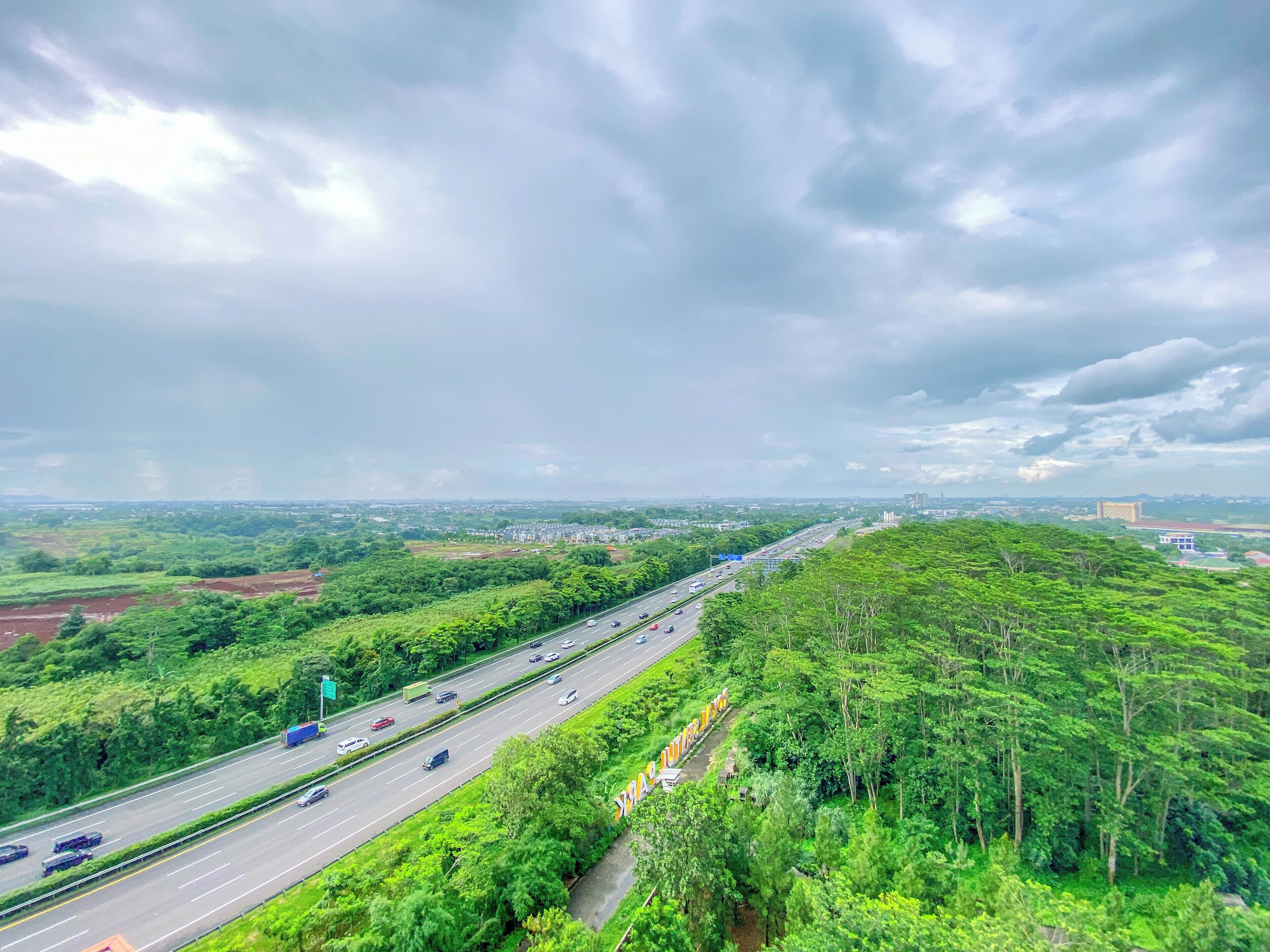 Eine Autobahn mit Fahrzeugen, umgeben von dichtem Grün und einem bewölkten Himmel.