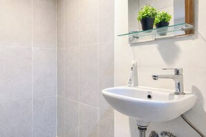 A bathroom with a white sink, chrome faucet, and a glass shelf with potted plants. - Neat Studio For 2 Pax At Royal Sentul Park Apartment (Bogor)