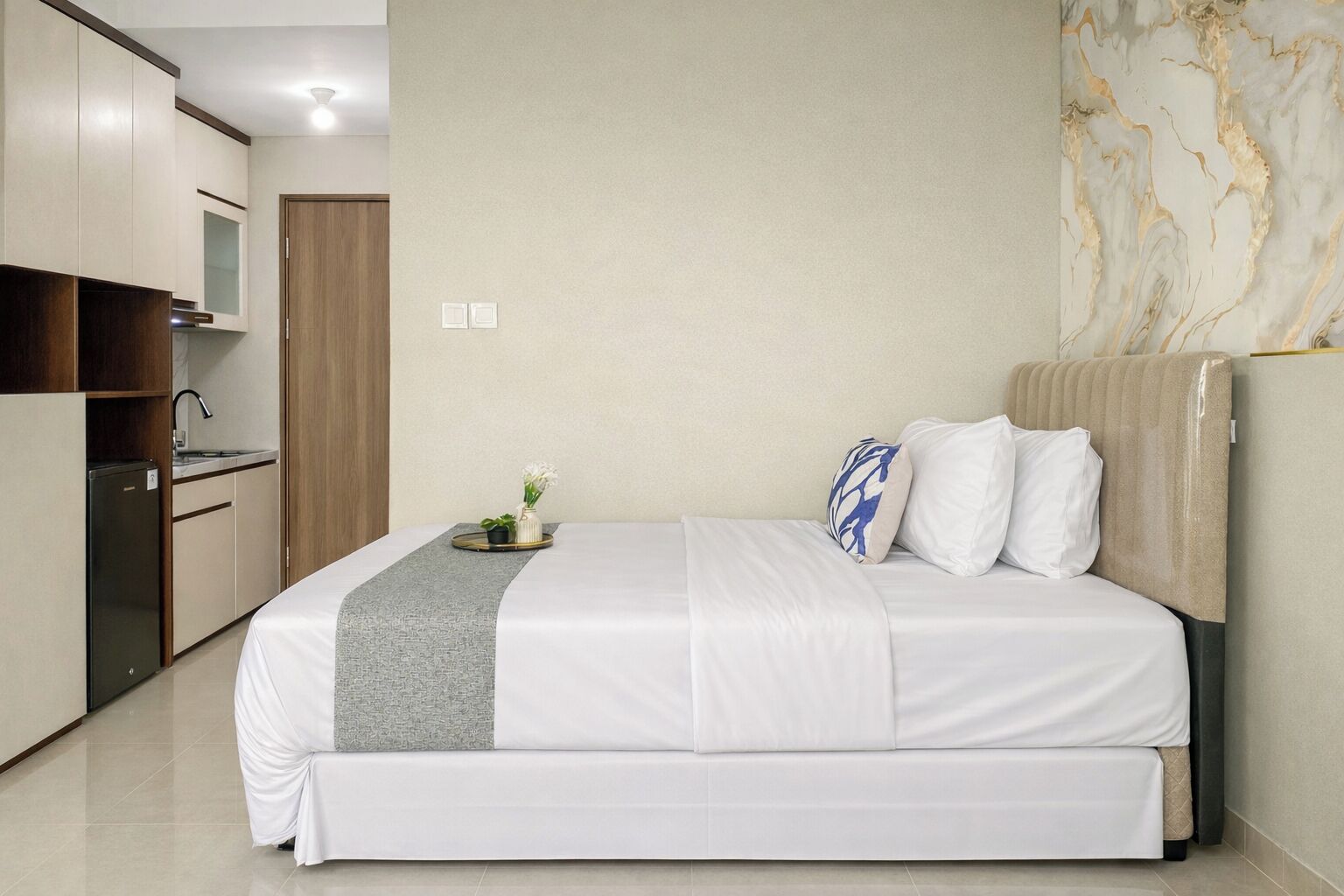 Habitación de hotel con cama, una pequeña cocina y una pared de mármol.